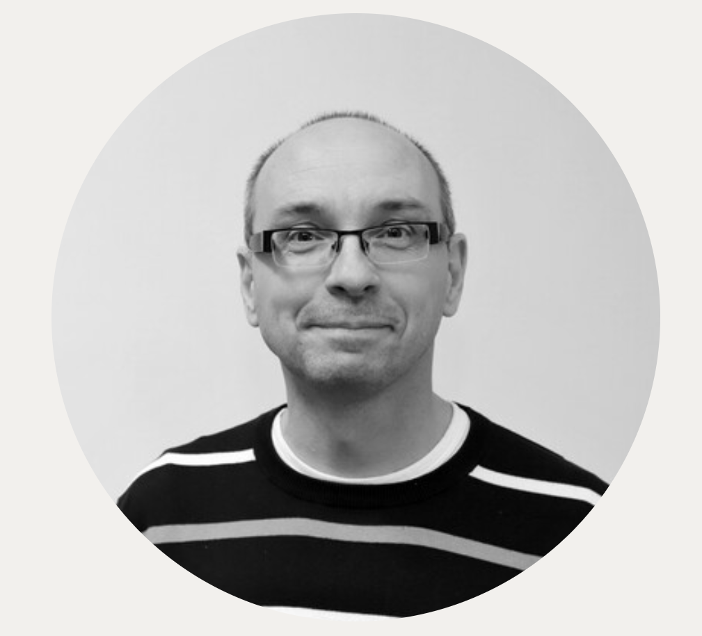 „Czarno‑białe, okrągłe zdjęcie mężczyzny w średnim wieku, z krótkimi włosami i okularami, w pasiastym swetrze, neutralne tło.